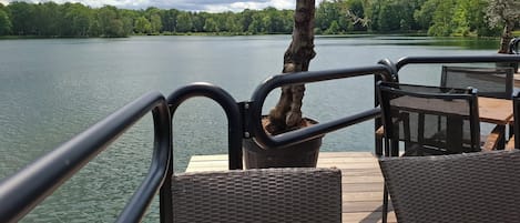 Une terrasse dotée de chaises en osier, donnant sur un lac, un arbre et un ciel nuageux.