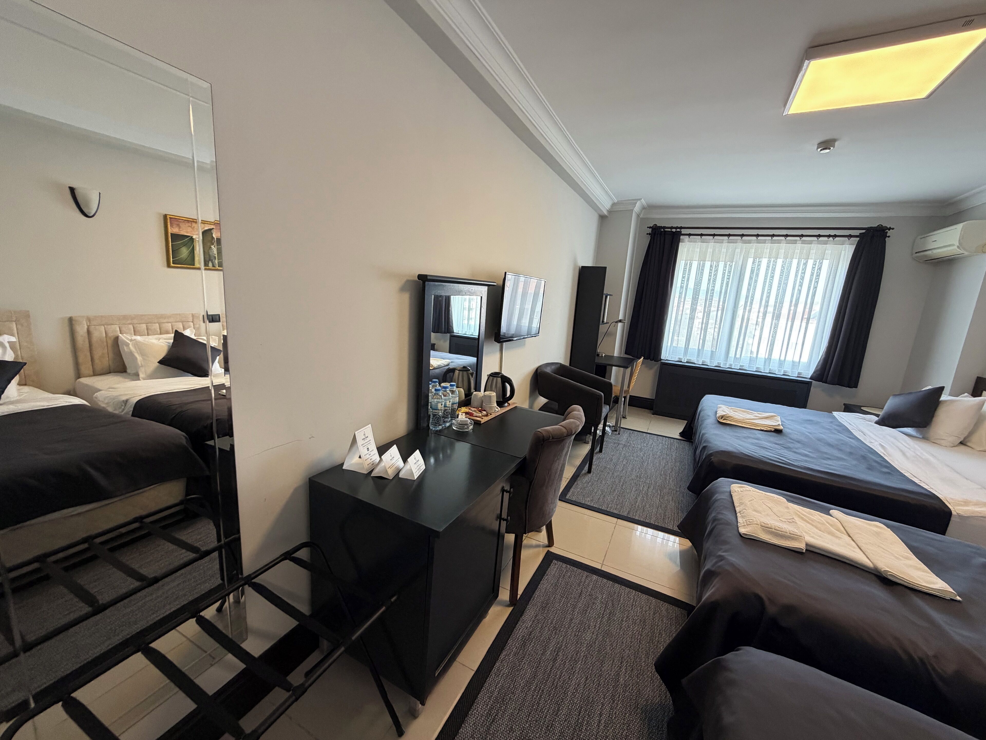 A hotel room with two beds, a desk, a chair, a TV, and a window with curtains.