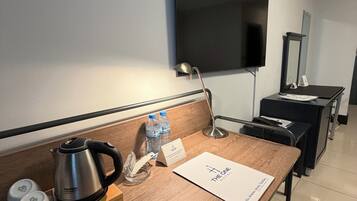 Een hotelkamer met een houten bureau, een waterkoker, flessenwater, een notitieboekje en een flatscreen televisie aan de muur.