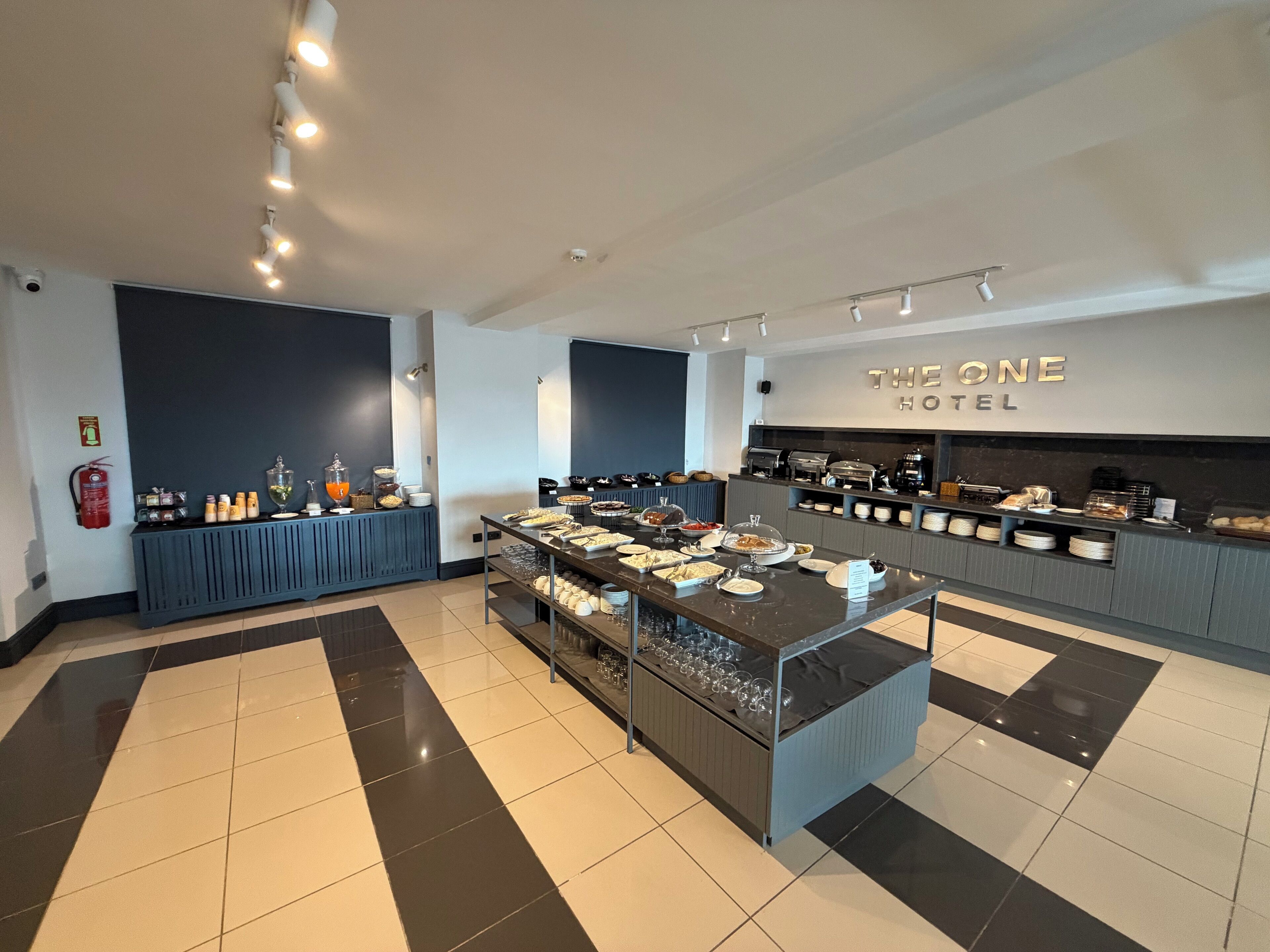 Zona de desayuno de hotel con estilo bufé, que incluye diferentes alimentos y bebidas, además de una estación de café.