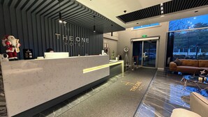A hotel reception area with a modern design, including a reception desk, a seating area with a sofa, and a large window offering a view of the outdoors. - THE ONE HOTEL (Kirsehir)