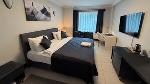 A hotel room with a bed, a desk, a chair, a TV, and a window with curtains. - THE ONE HOTEL (Kirsehir)