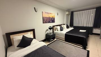 A hotel room with two beds, a nightstand, a lamp, a painting, and a window with curtains.