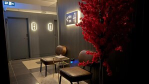 A modern lobby with a reception desk, two chairs, a small table, and a decorative red plant. - THE ONE HOTEL (Kirsehir)