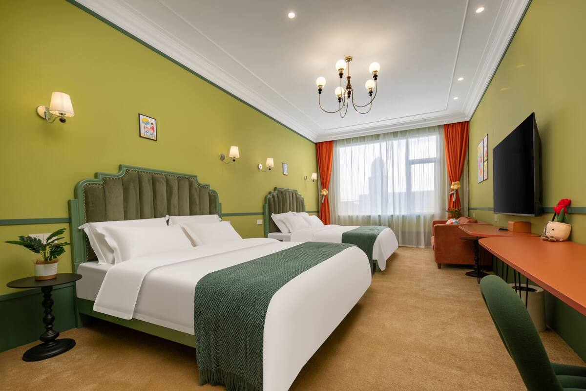 A hotel room with two beds, a desk, a chair, a television, and a window with curtains.