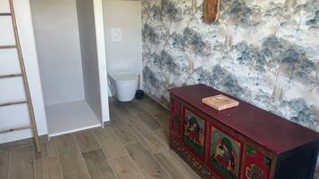 Et badeværelse med toilet, trægulv, rødt skab med kunst og væg med træmotiv.