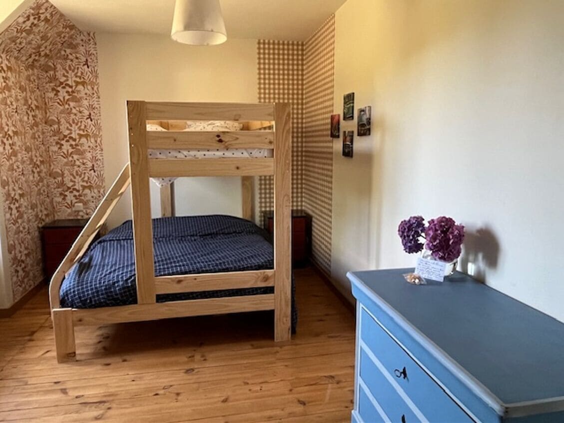 Een houten stapelbed in een kamer met een blauwe dressoir en een wandplank met bloemen.