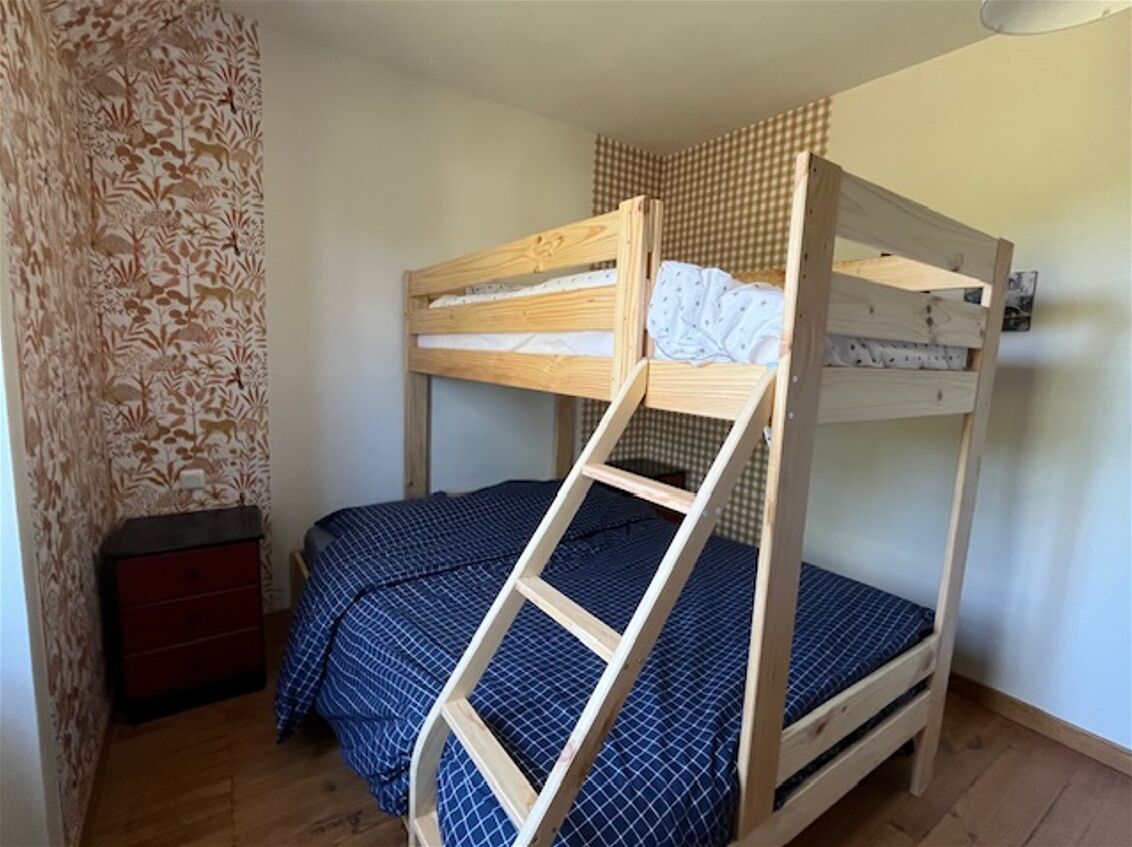 A bunk bed with a ladder, a small red dresser, and patterned wallpaper.