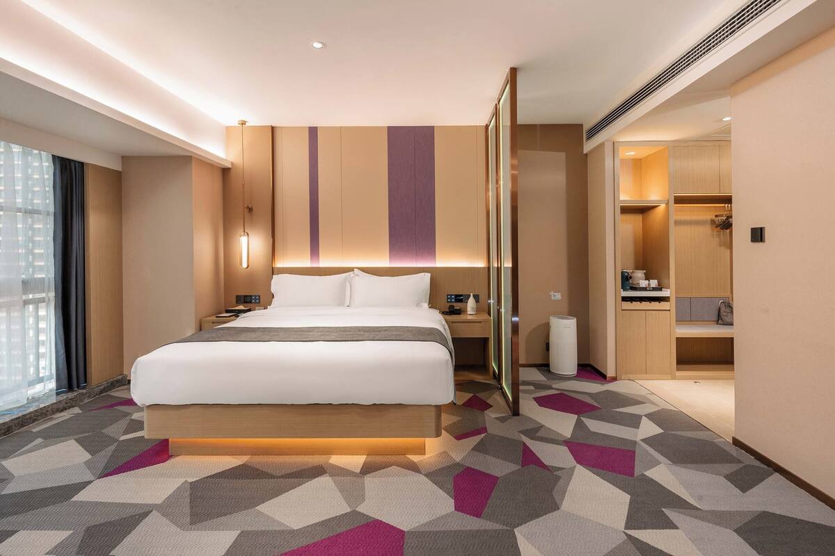 Habitació d'hotel moderna amb un llit gran, taules de nit, un armari encastat i vistes a la ciutat.