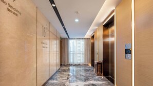 Un pasillo de hotel con piso de mármol, un cartel de prohibido fumar y un ascensor.