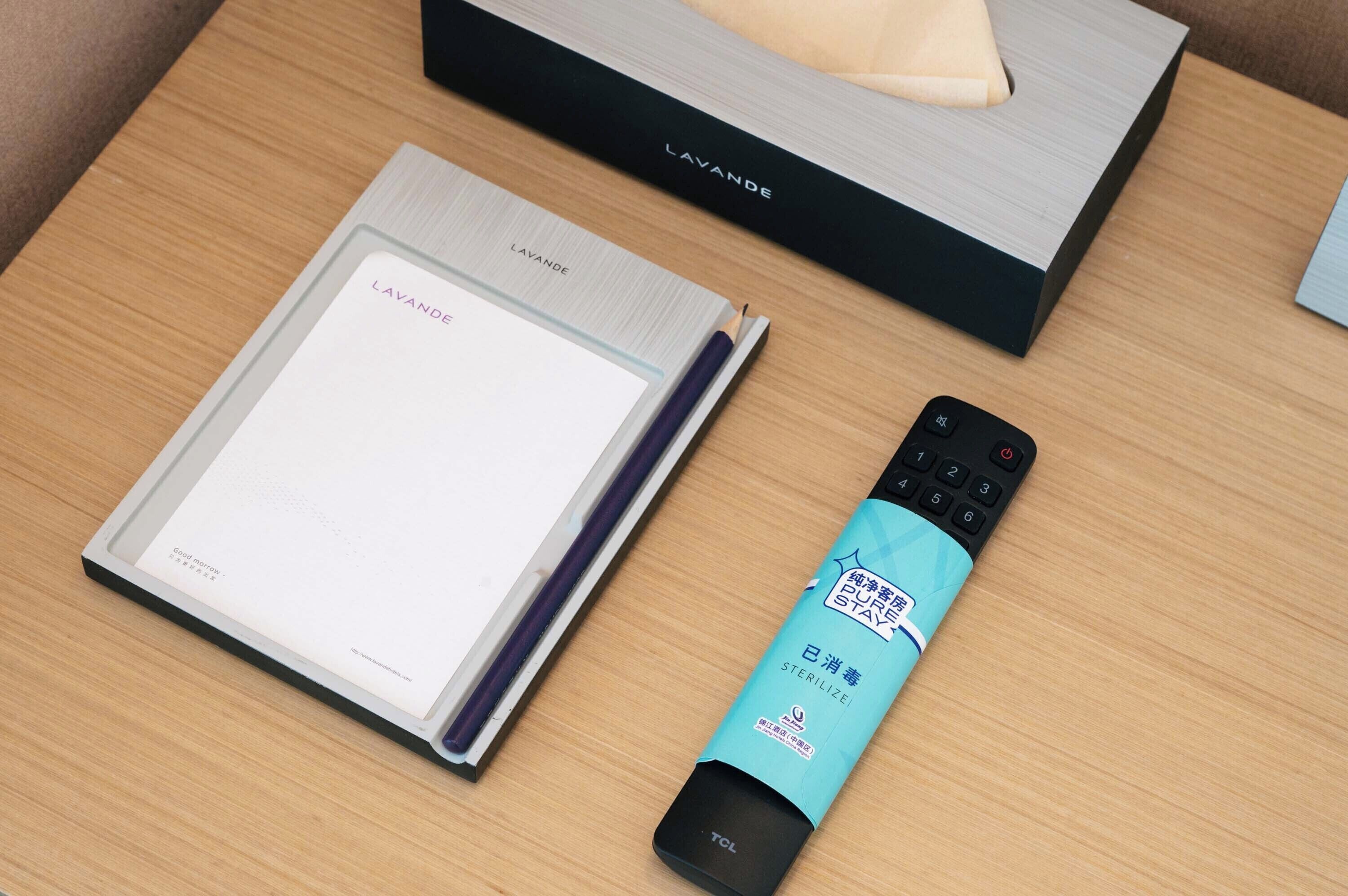 A notebook, a remote control, and a tissue box on a wooden surface.