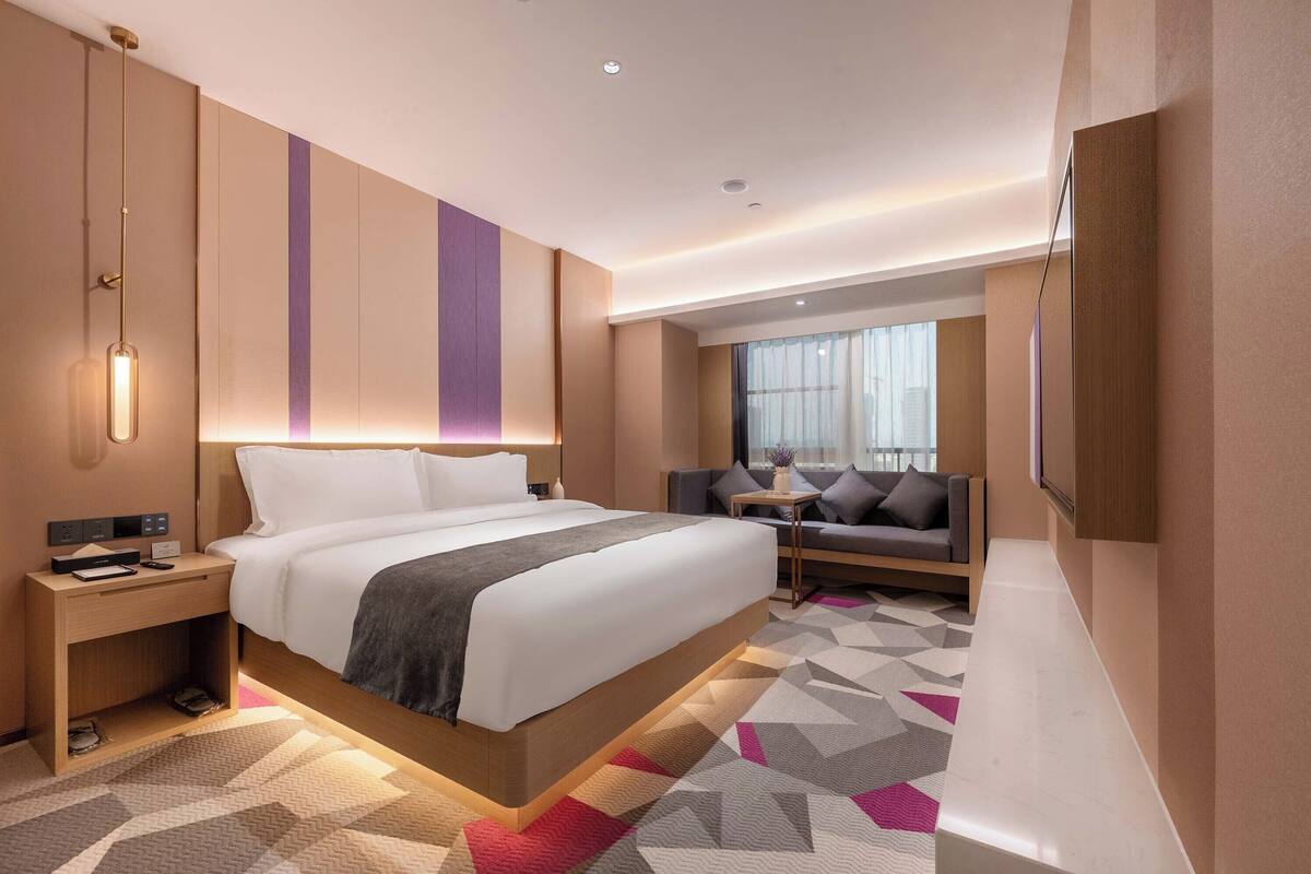 Una habitació d'hotel moderna amb un llit gran, una taula de nit i una zona de seients amb un sofà.