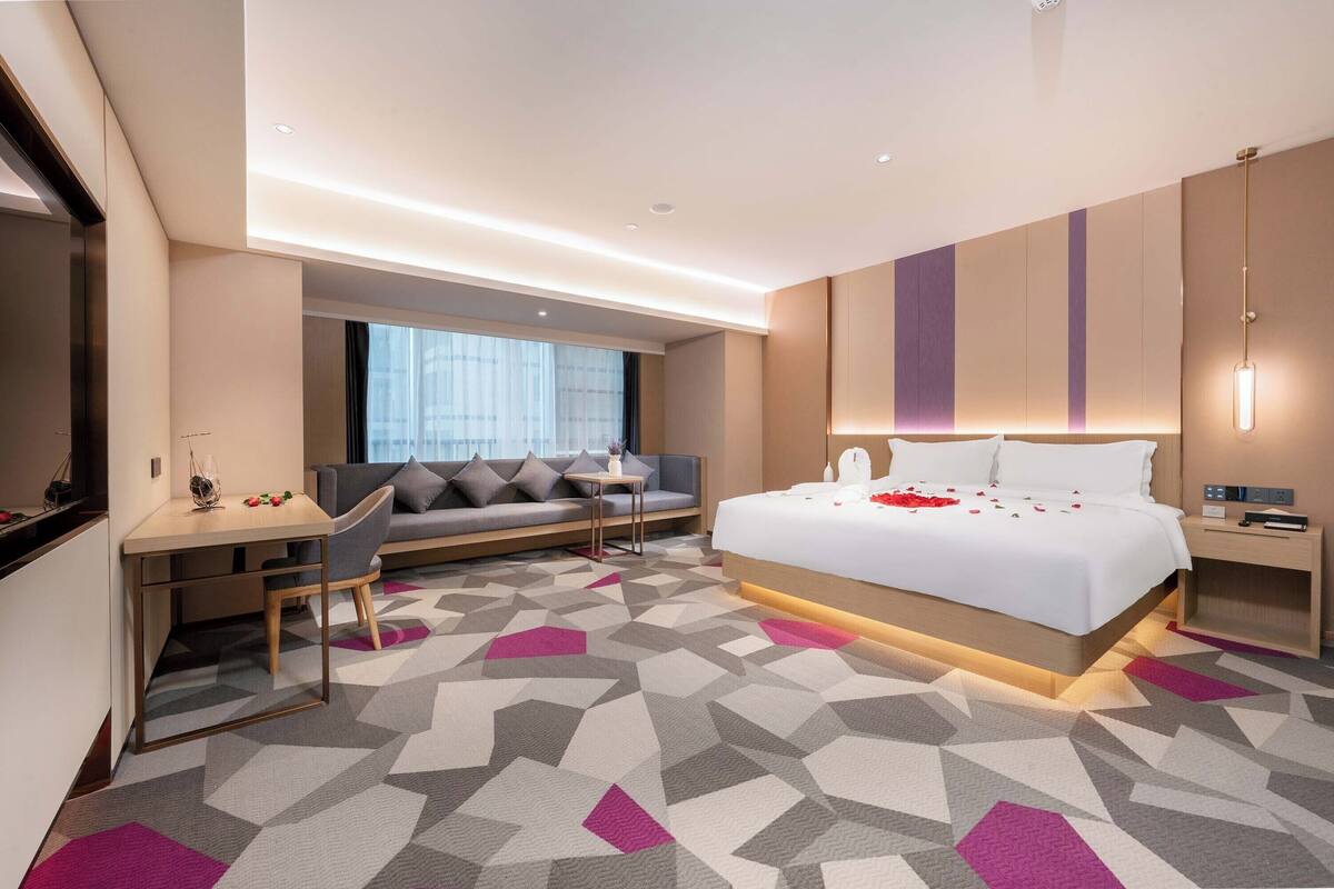 Habitació d'hotel moderna amb un llit gran, un escriptori, un sofà i vistes a la ciutat.