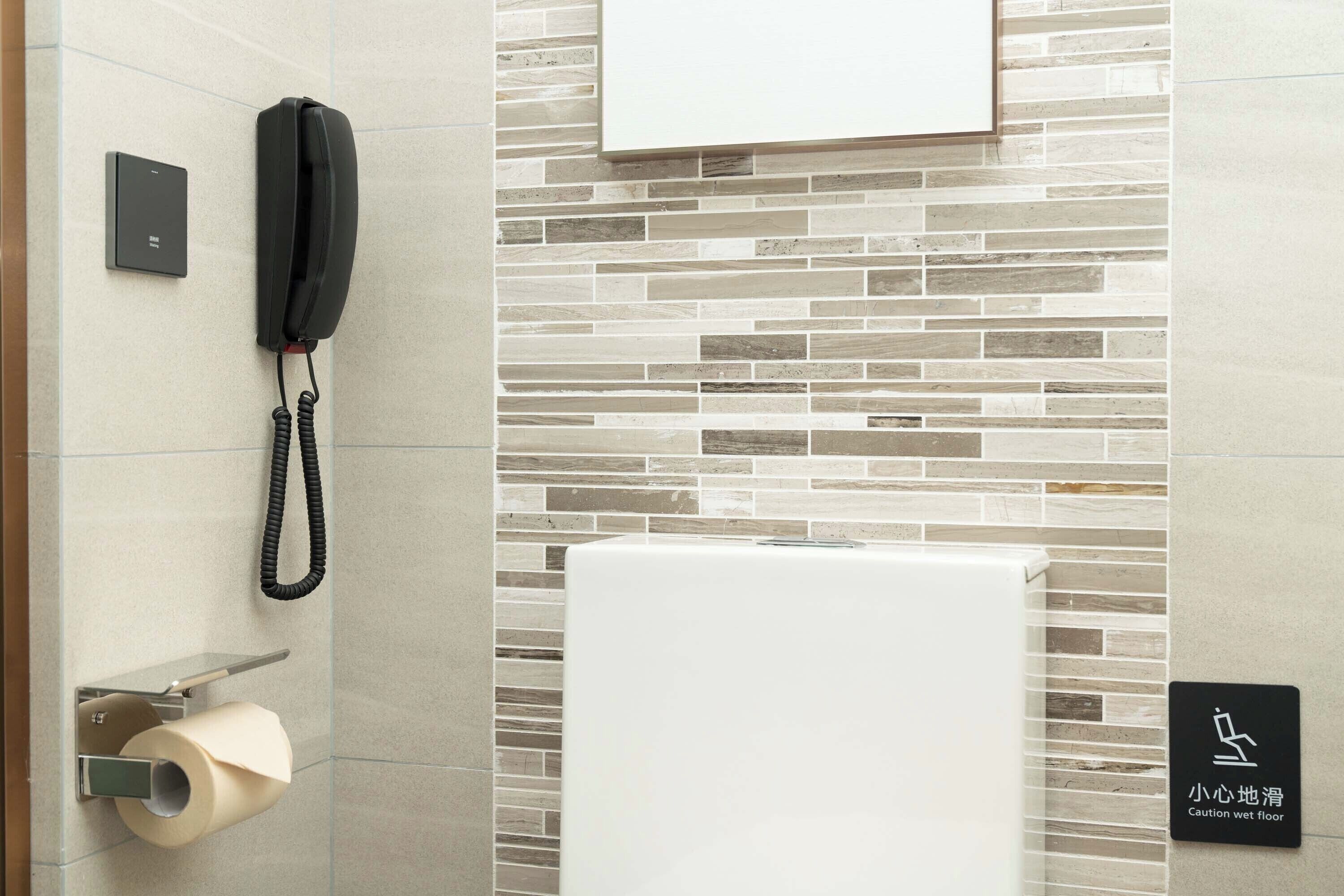 Ein Badezimmer mit Toilettenpapierhalter, Telefon und Piktogramm für nassen Boden.