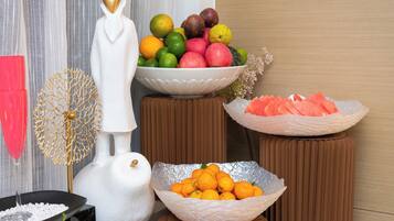 A room with a white statue, a bowl of oranges, a bowl of apples, and a bowl of watermelon.