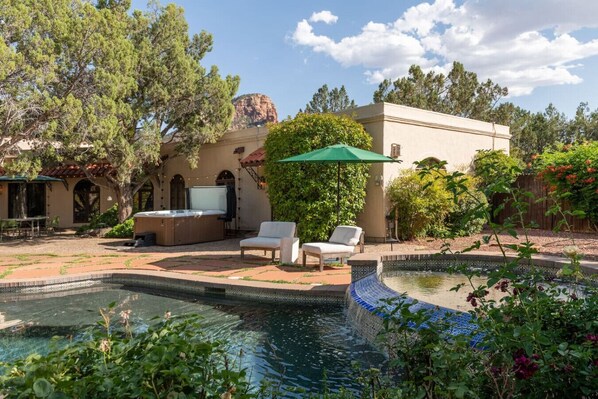 A pool area with a hot tub, lounge chairs, and a pergola with a green umbrella.