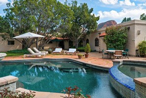 A pool with lounge chairs and a patio area with tables and chairs.