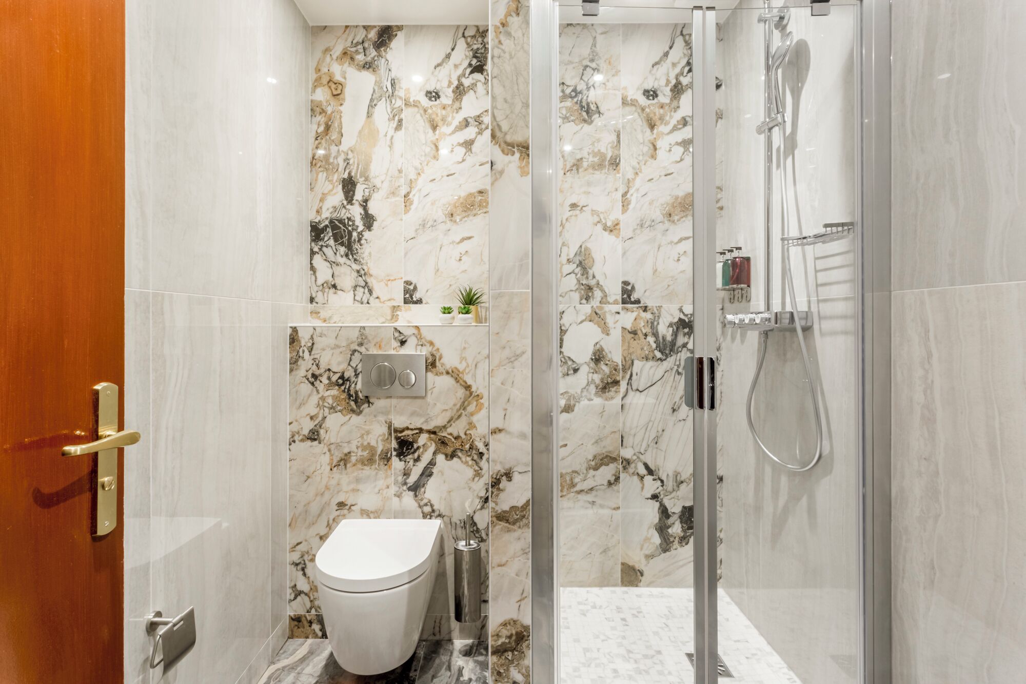Un baño con inodoro, ducha de mampara de vidrio y paredes de mármol.