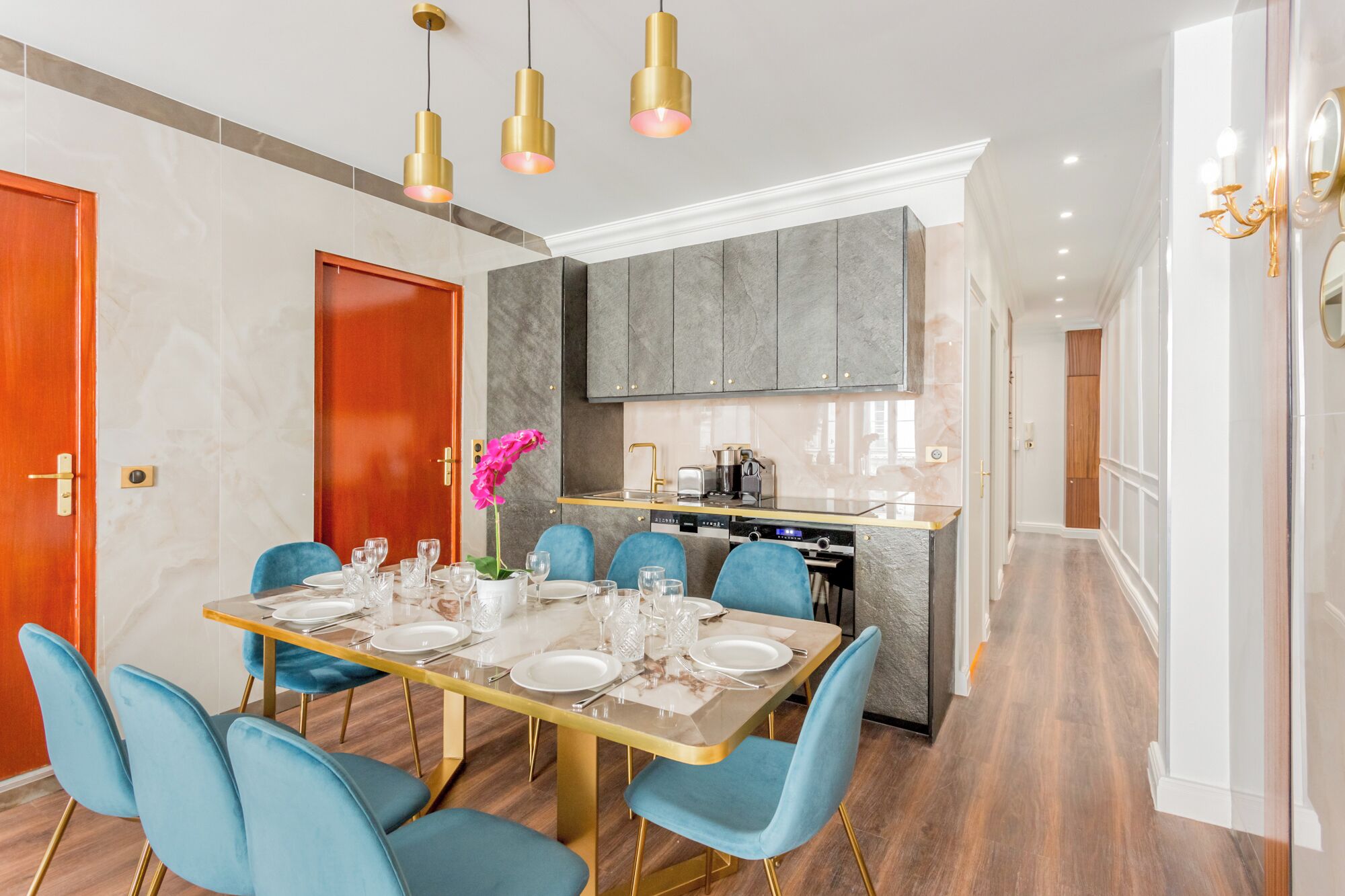 Un comedor moderno con una larga mesa dispuesta para seis personas, sillas azules y detalles dorados.