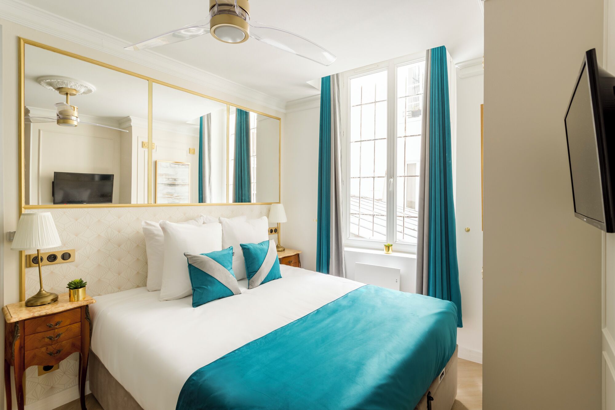 Une chambre d’hôtel avec un grand lit, un miroir, une télévision et une fenêtre avec des rideaux.