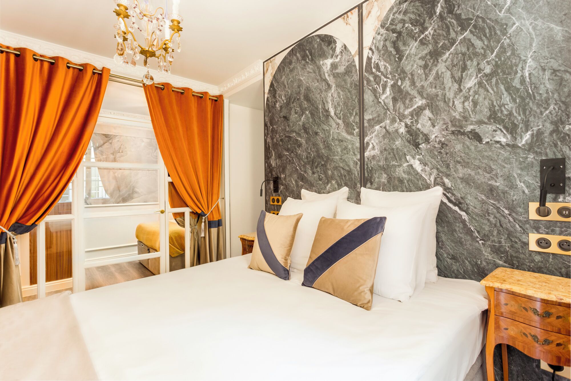 A bedroom with a large bed, orange curtains, a marble wall, and a wooden nightstand.