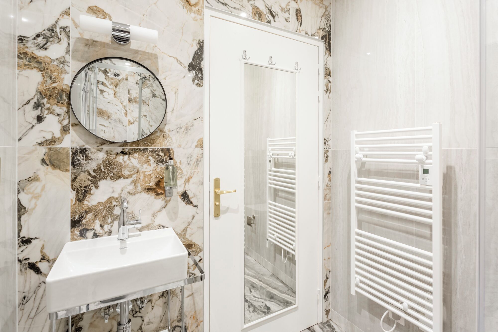 A bathroom with a marble sink, a mirror, a towel rack, and a glass shower enclosure.