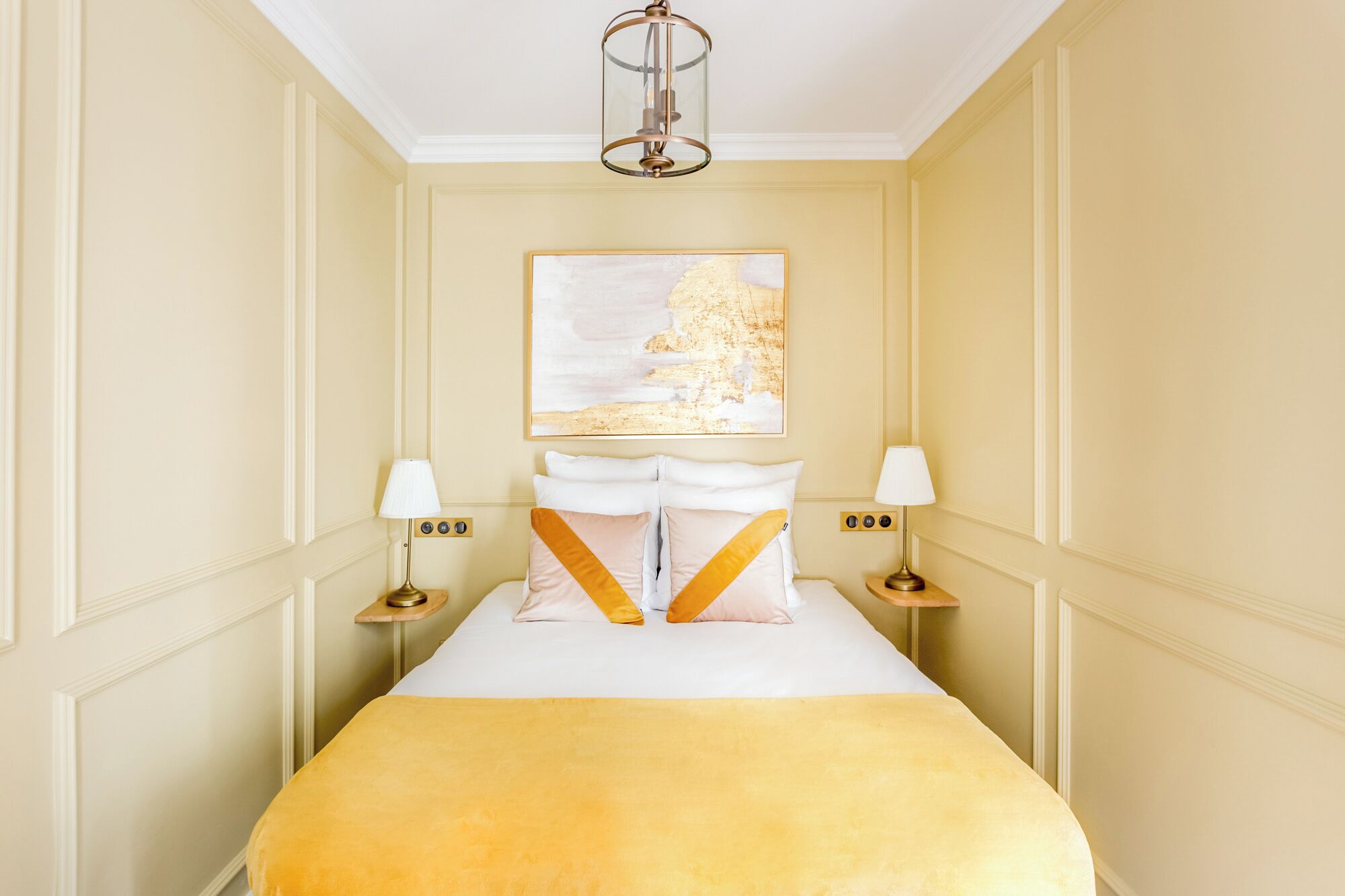 A hotel room with a bed, two bedside tables with lamps, a painting on the wall, and a ceiling light fixture.
