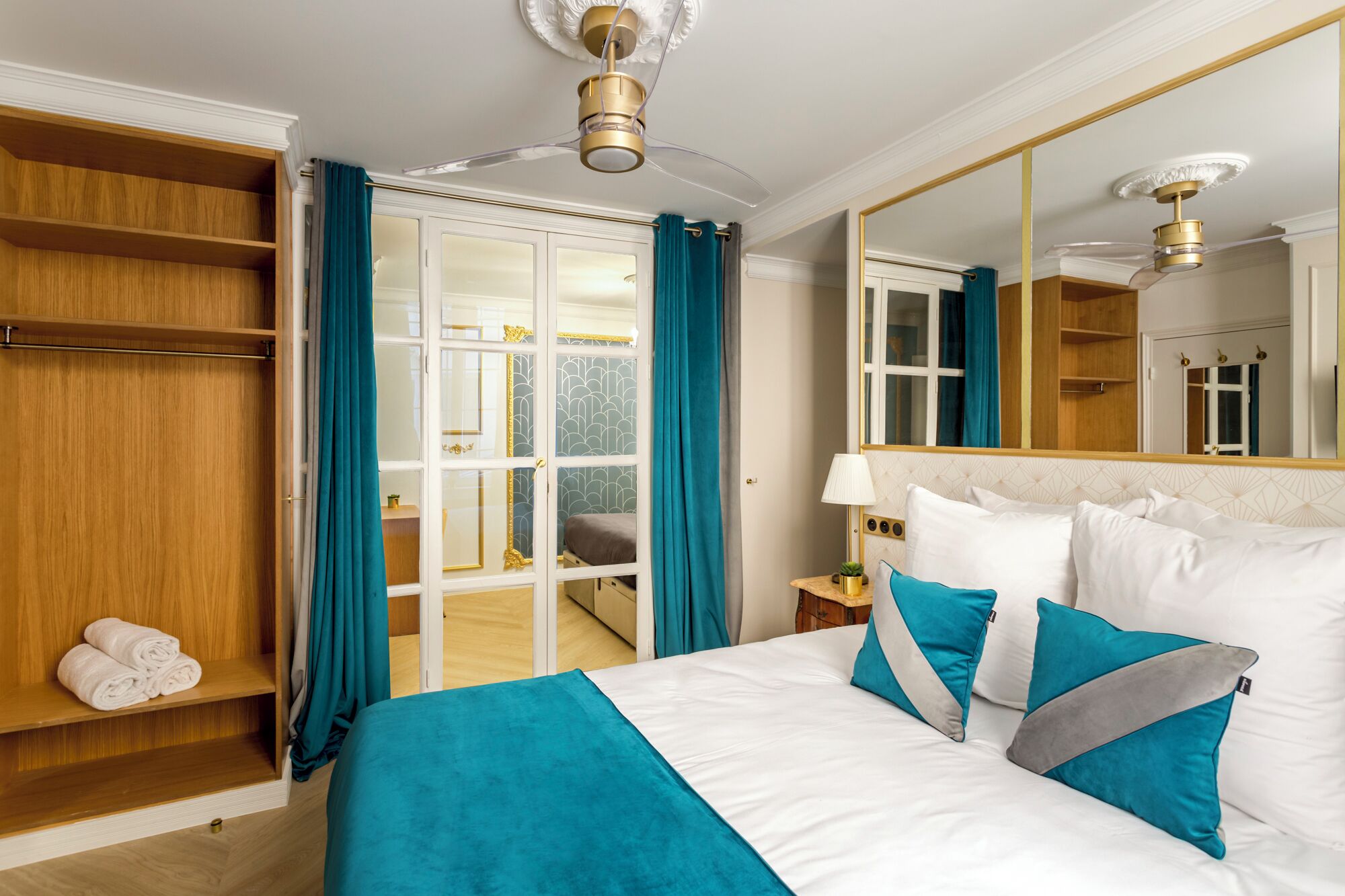 A hotel room with a bed, a wardrobe, a mirror, and a ceiling fan.