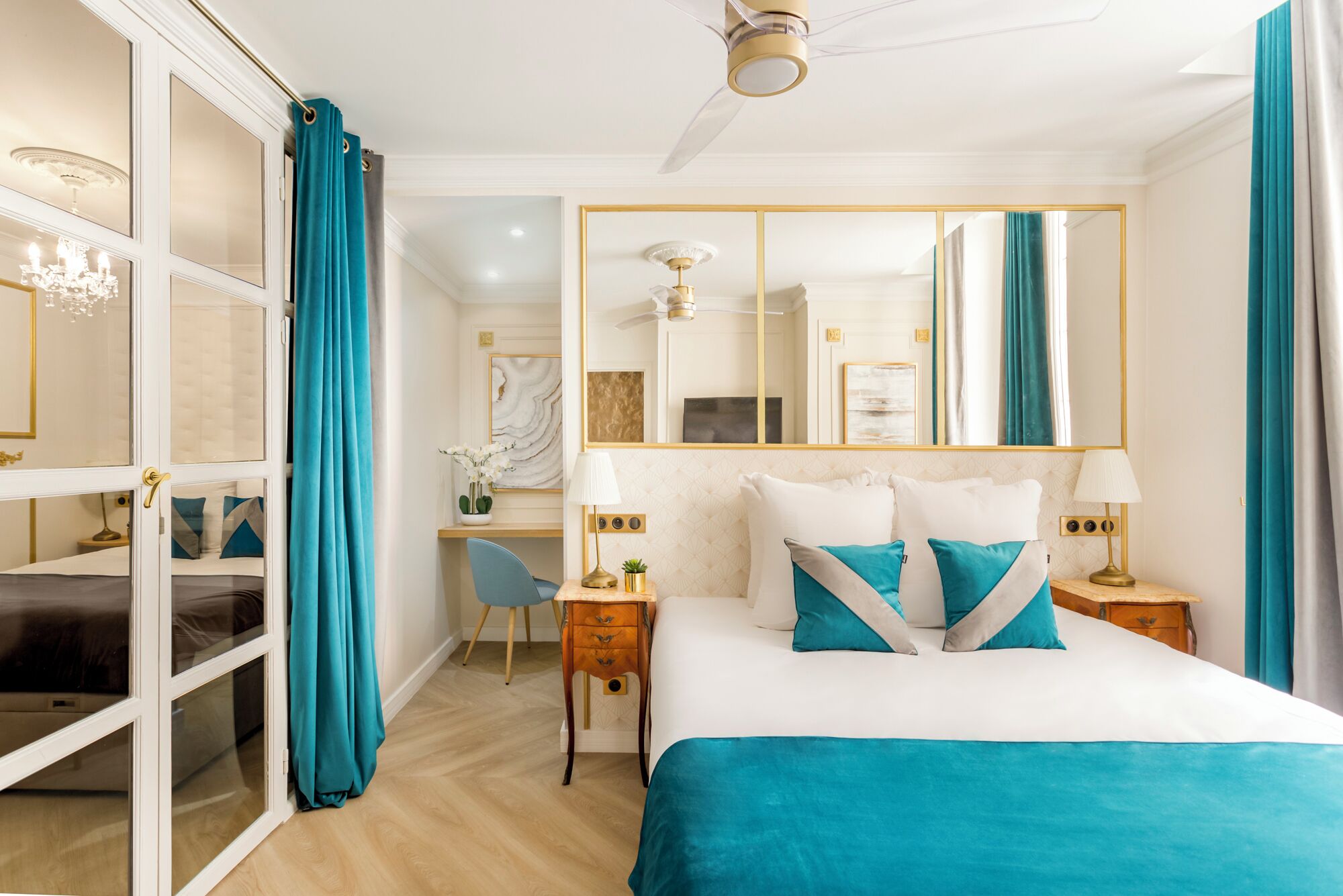 Une chambre d’hôtel équipée d’un lit, d’un bureau, d’une chaise, d’un miroir et d’un ventilateur de plafond.