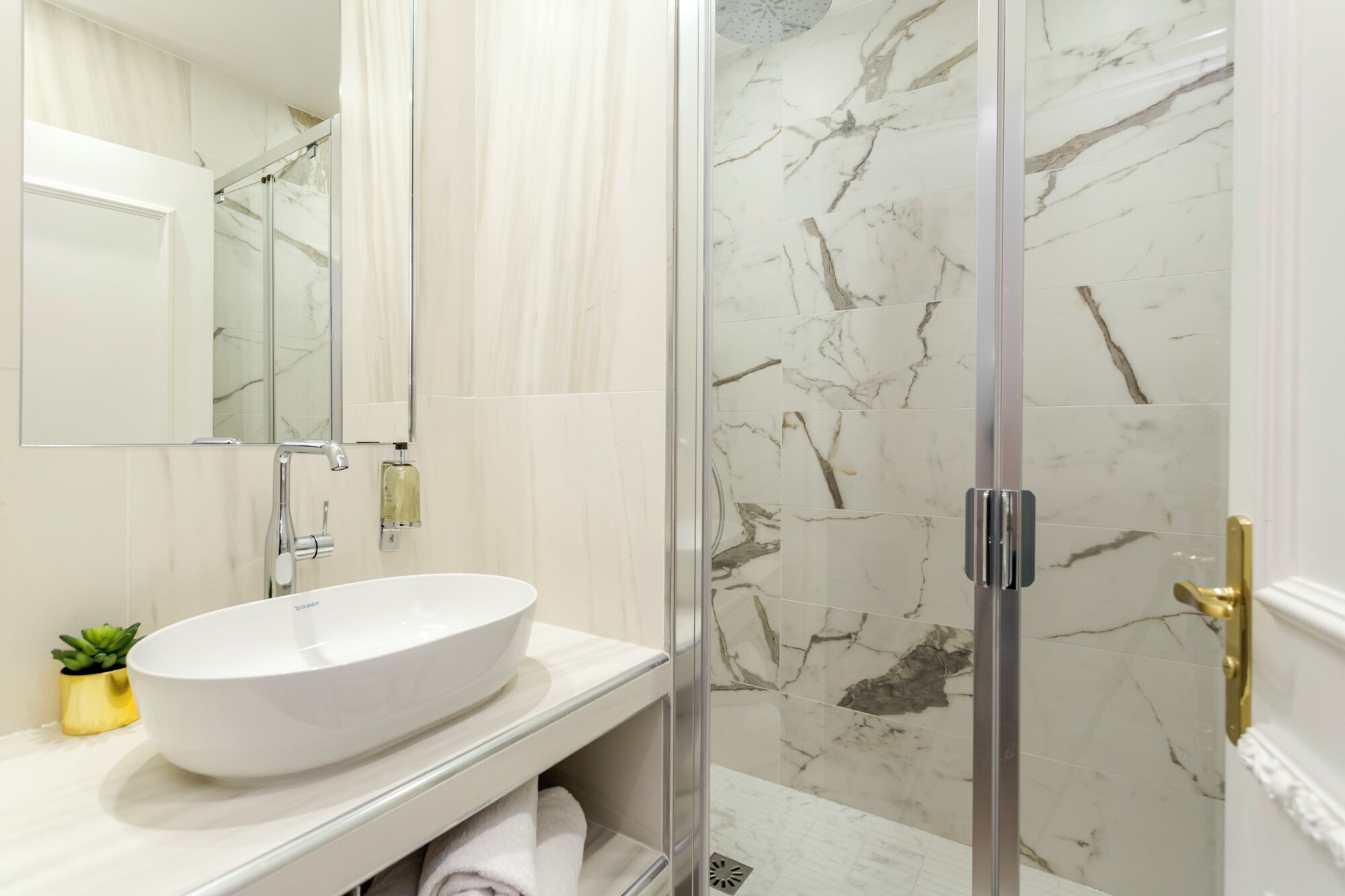 A bathroom with a white sink, a mirror, and a shower with marble tiles.