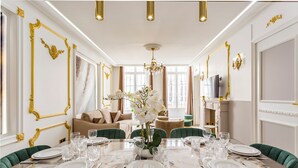 A dining room with a marble table set for six, gold accents on the walls, and a chandelier. - Merveil Luxury Suites - Marais - Martin I-II (Paris)
