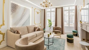 A modern living room with a beige sofa, a round coffee table, and a green ottoman. - Merveil Luxury Suites - Marais - Martin I-II (Paris)