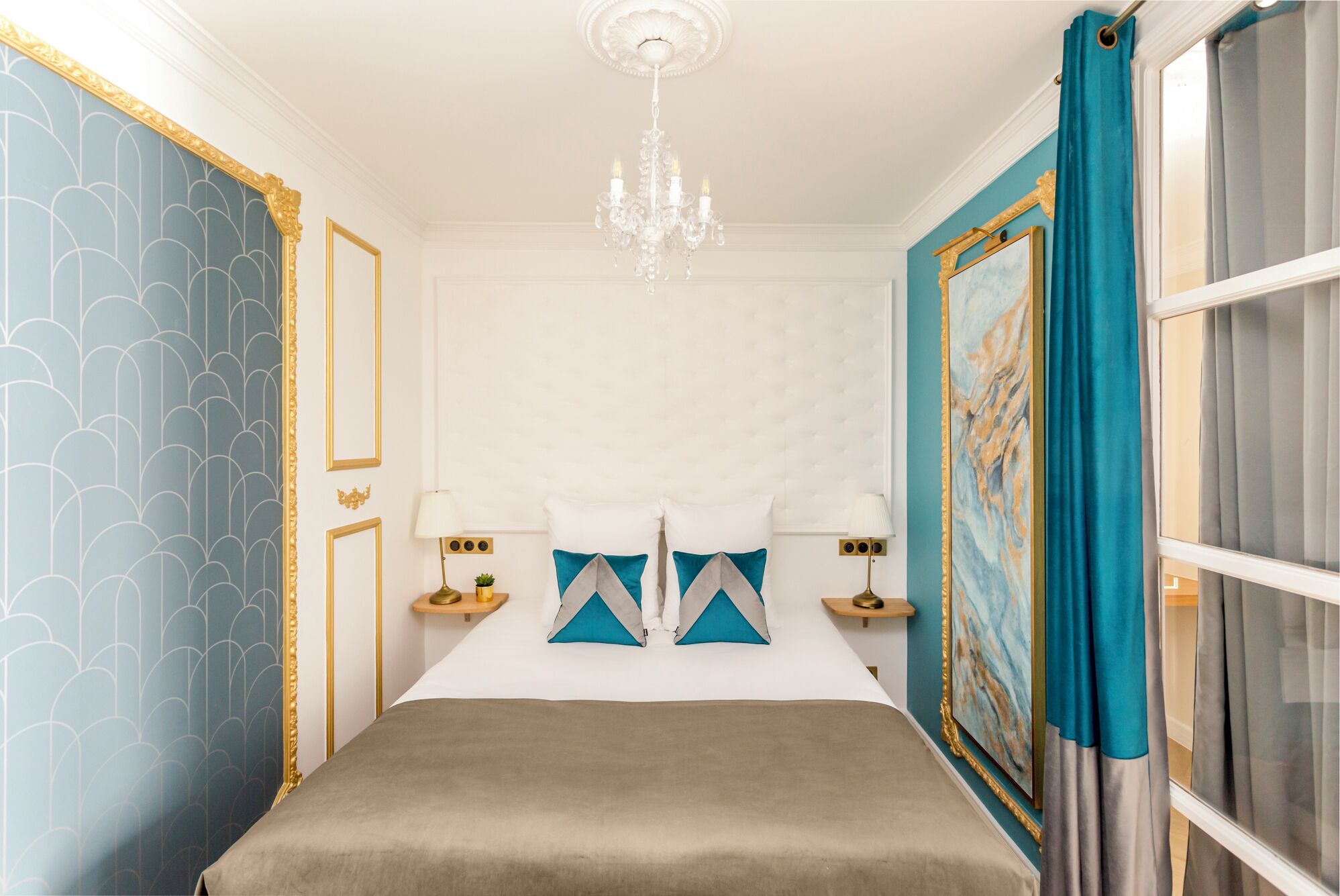 A bedroom with a large bed, a chandelier, and a painting on the wall.