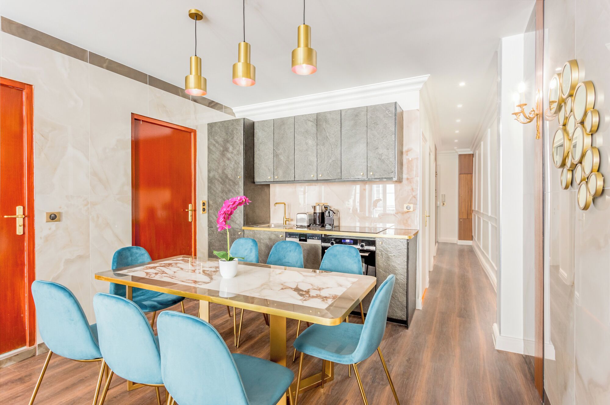 A modern kitchen with a central island, blue chairs, and gold pendant lighting.