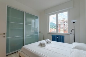 A hotel room with a bed, a window with a view of buildings, a radiator, and a wardrobe. - Spacious flat with Balcony (Sestri Levante)