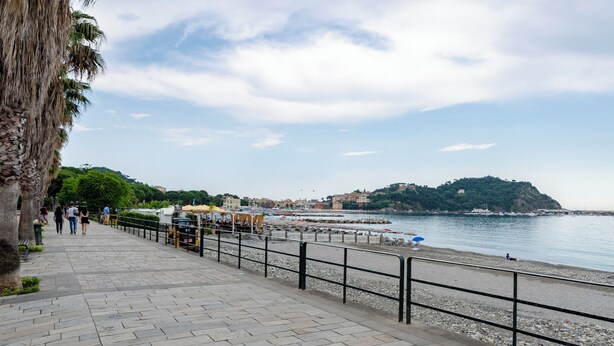 A paved walkway along a waterfront with a railing, a beach, and a distant hill with buildings. - Spacious flat with Balcony (Sestri Levante)