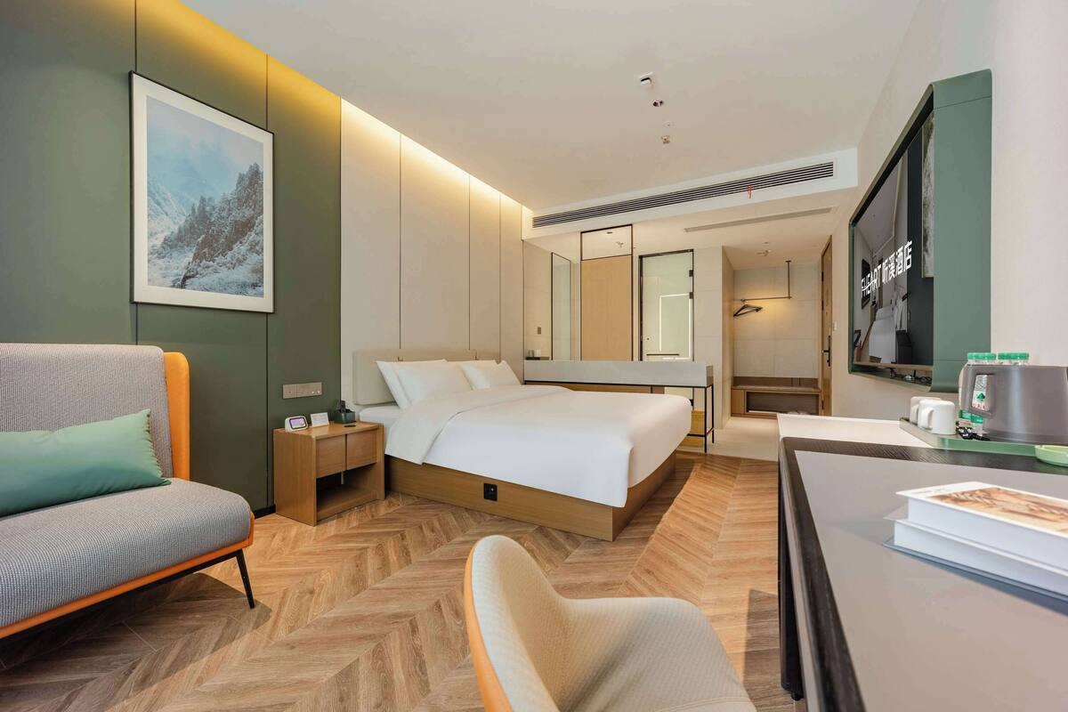 A modern hotel room with a bed, a sofa, a desk, and a large mirror.