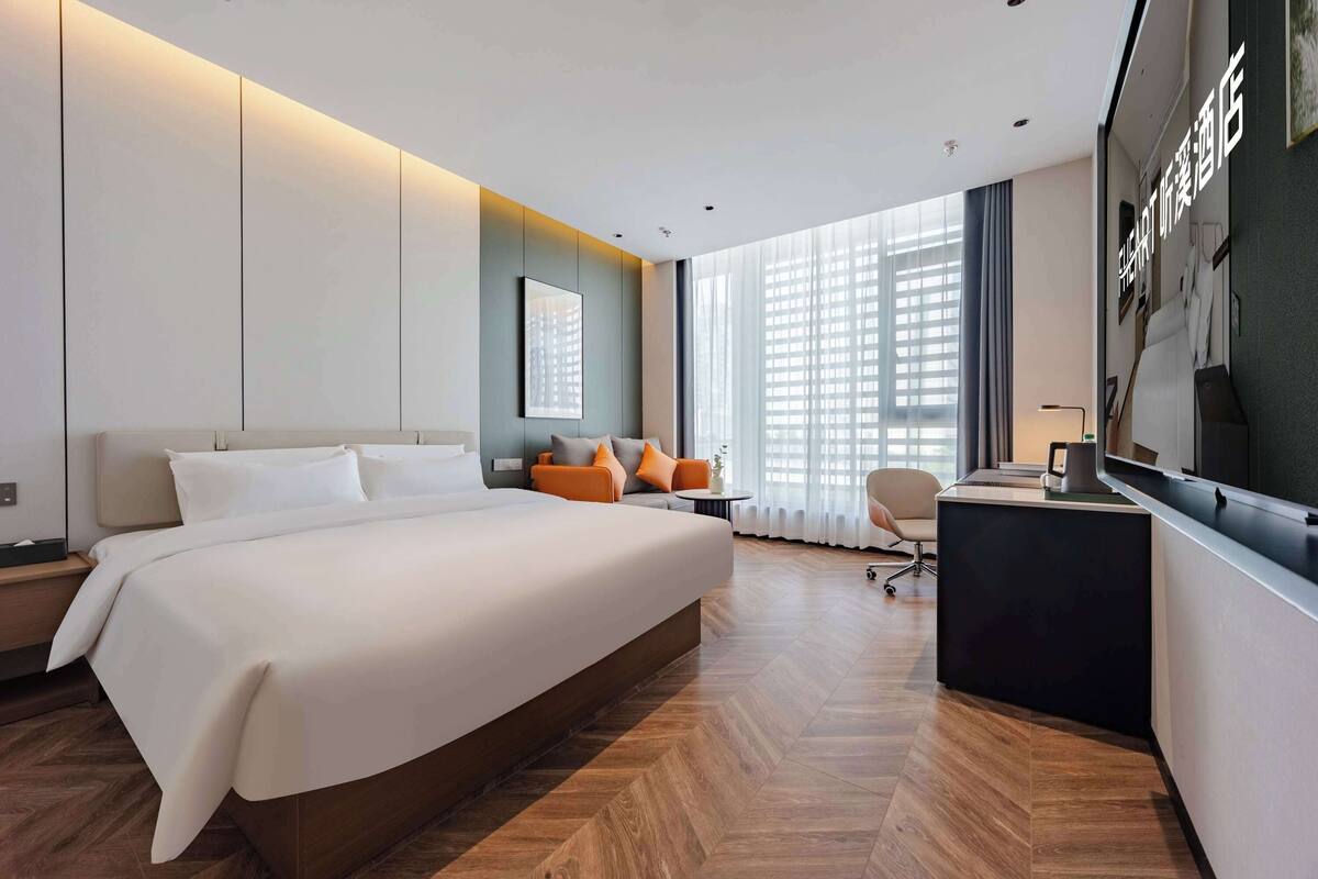 A modern hotel room with a large bed, a desk, and a view of the city.