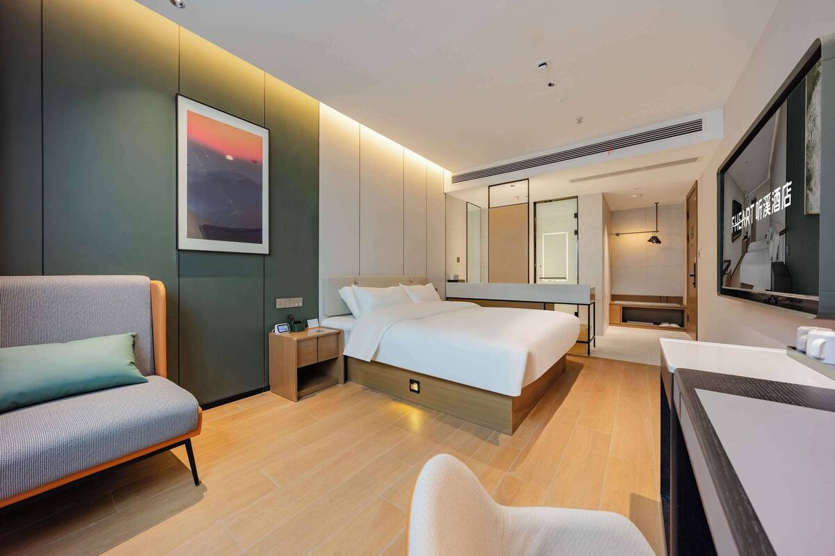 A modern hotel room with a bed, a sofa, a desk, and a large mirror.