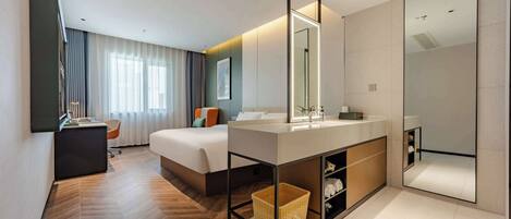 A modern hotel room with a large bed, a vanity with a mirror, a small desk, and a wicker basket.