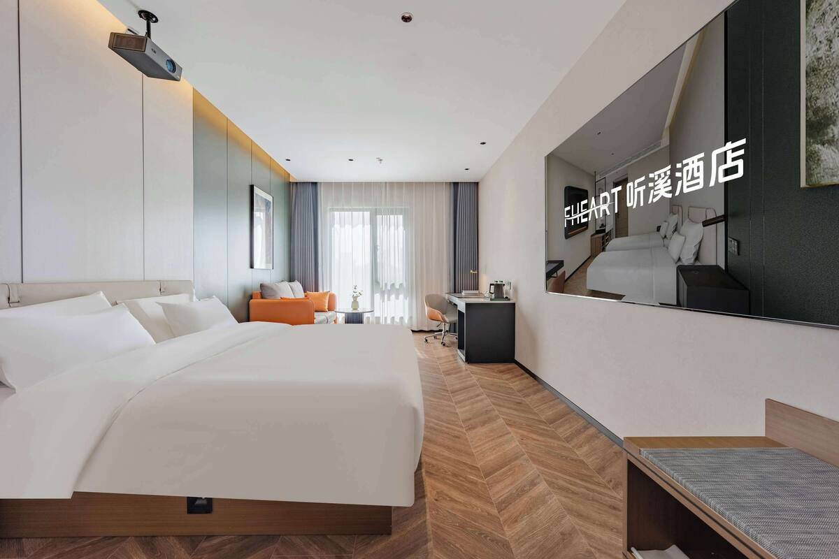 A modern hotel room with a large bed, a desk, and a seating area.