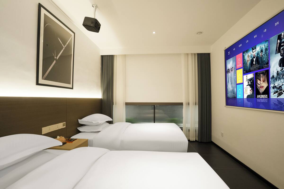 A hotel room with two beds, a large poster on the wall, and a window with curtains.