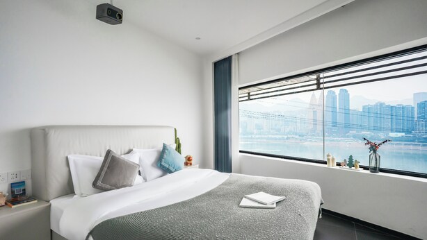 A modern hotel room with a large bed, a view of a city skyline, and a projector mounted on the ceiling. - Time Wharf Hotel - Jiefangbei Shibati (Chongqing)