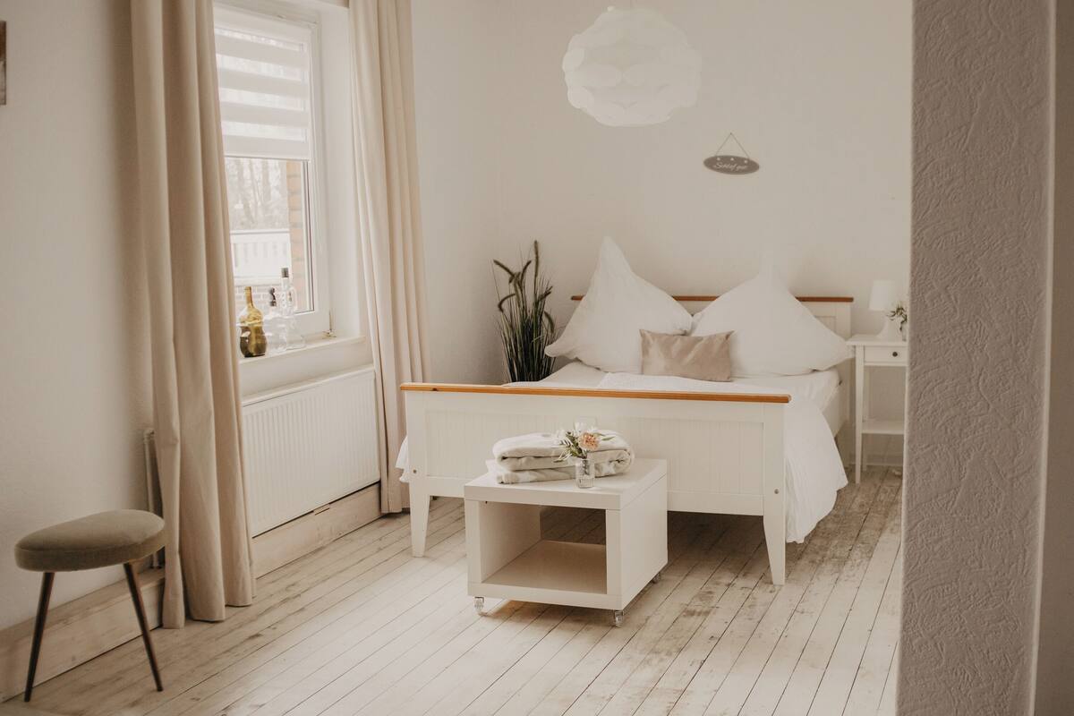 A bedroom with a wooden bed, a bedside table, a window with curtains, and a radiator.