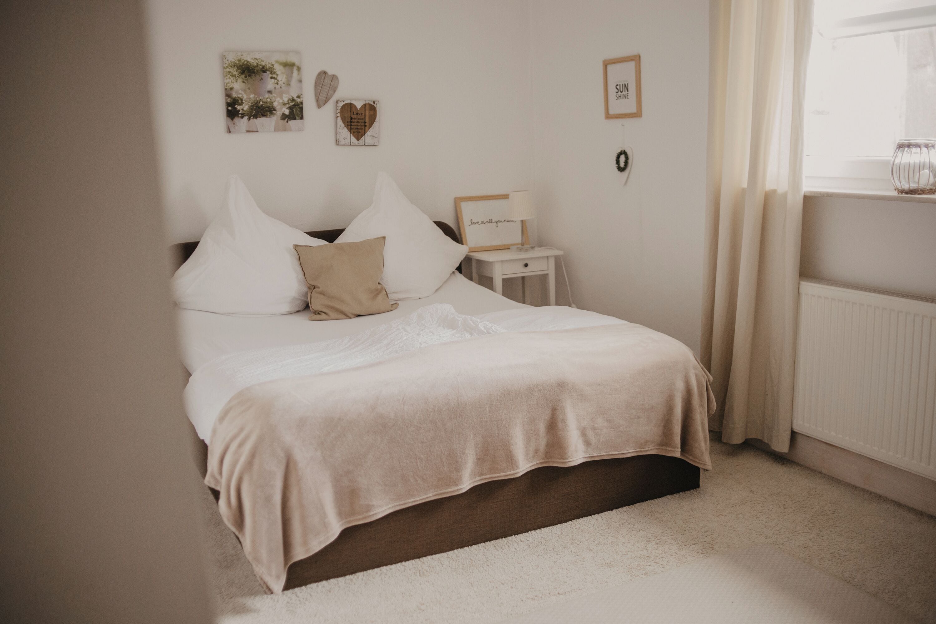A bedroom with a bed, a nightstand, a wall-mounted shelf, and a window with curtains.