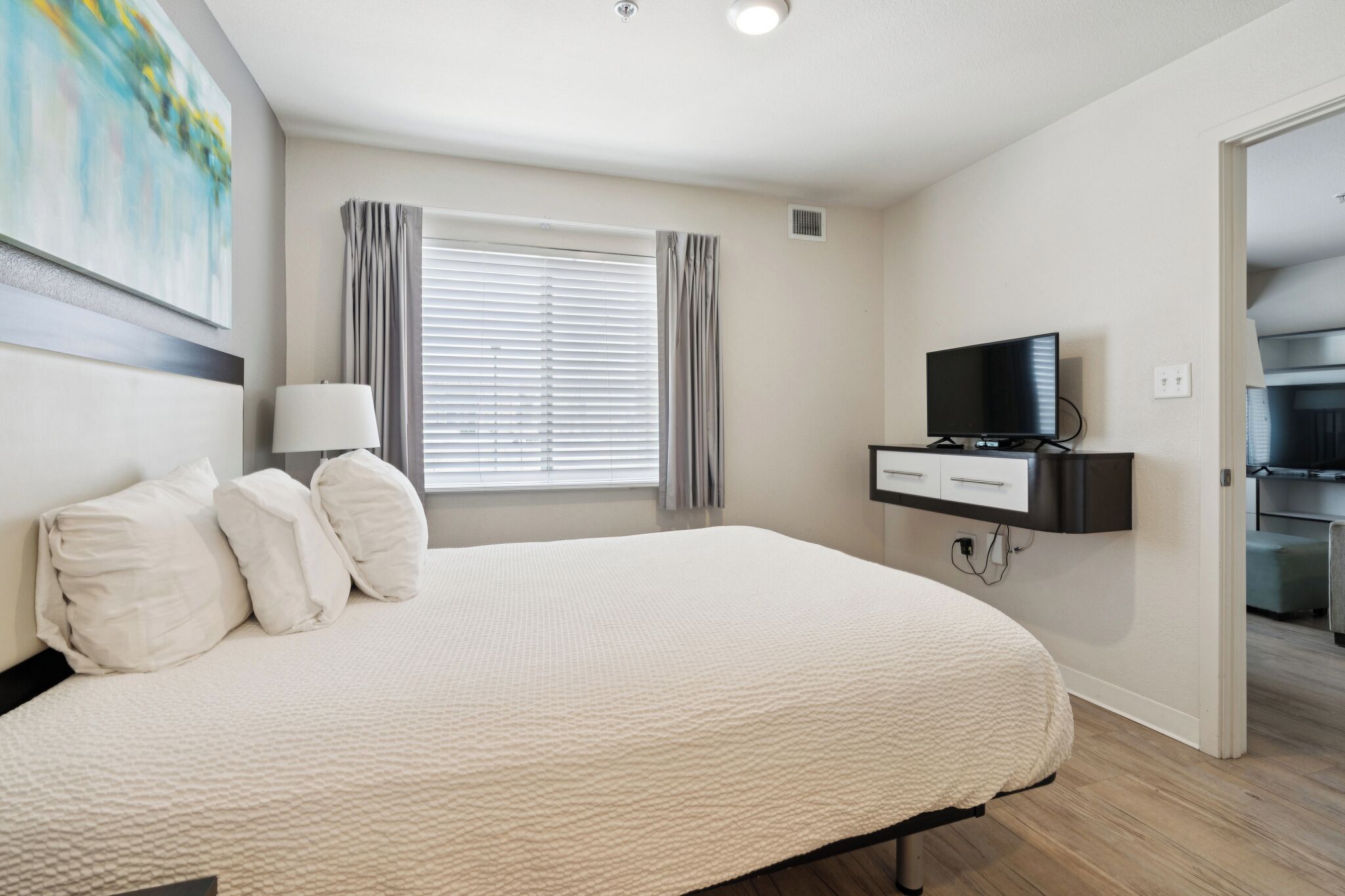 Une chambre à coucher avec un lit, une télévision, un bureau et une fenêtre avec des rideaux.