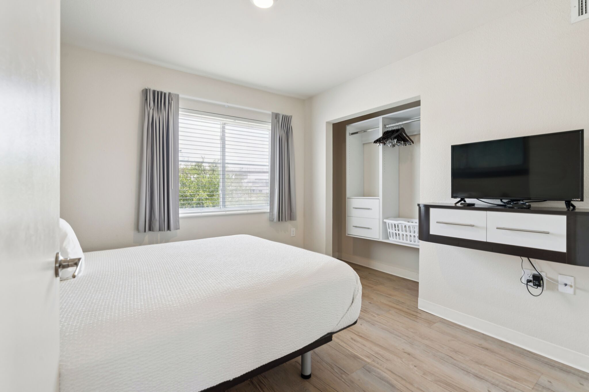 A hotel room with a bed, a TV, a mirror, and a window with curtains.
