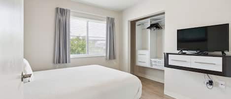 A hotel room with a bed, a TV, a mirror, and a window with curtains.