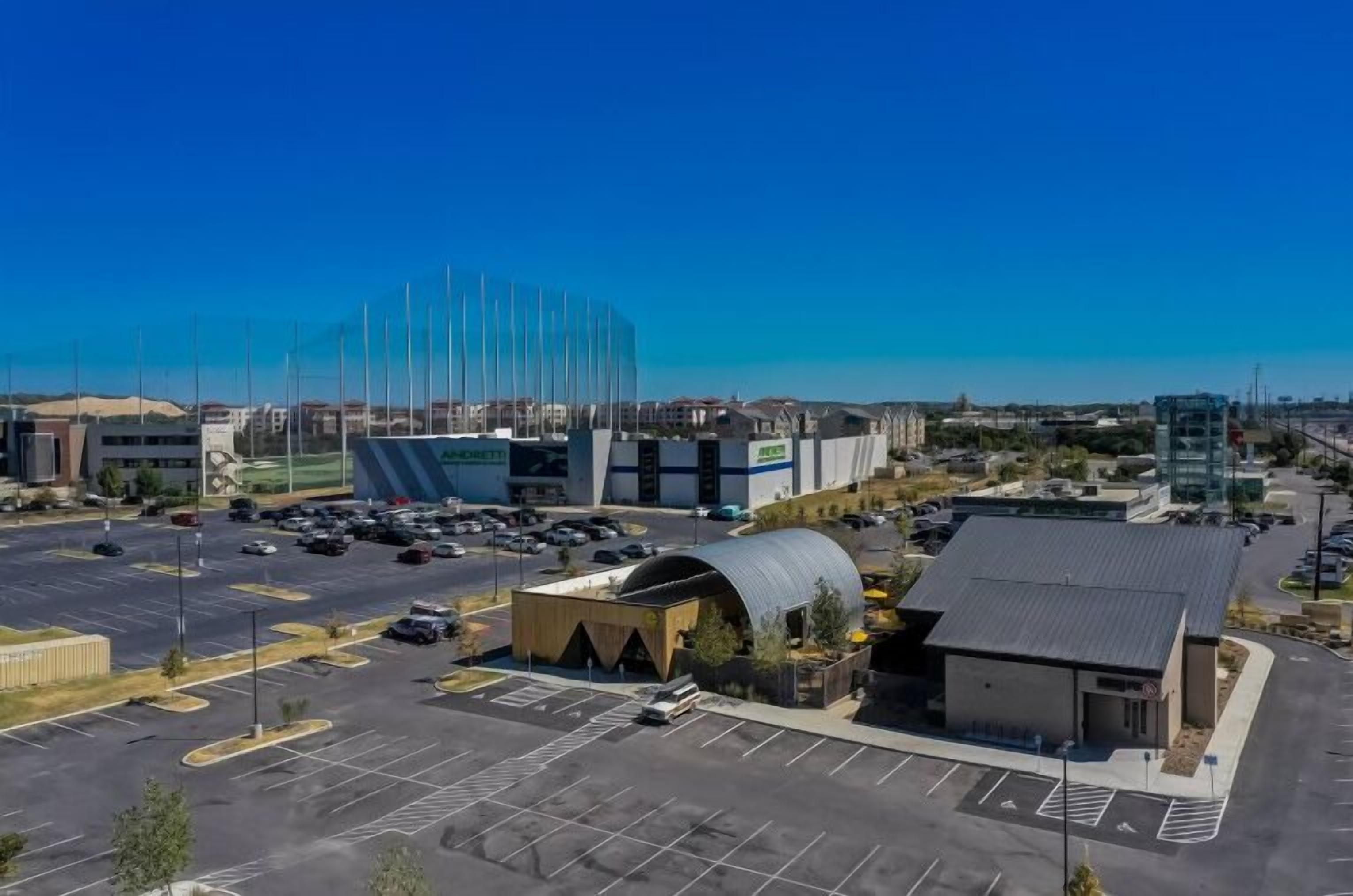 An aerial view of a commercial area with a large building, parking lots, and a smaller structure with a curved roof.