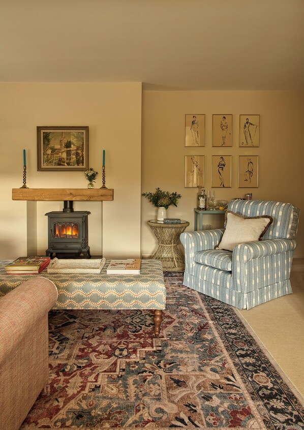 Un salon chaleureux avec un poêle à bois, un tapis à motifs, un fauteuil et des œuvres d’art encadrées accrochées au mur.